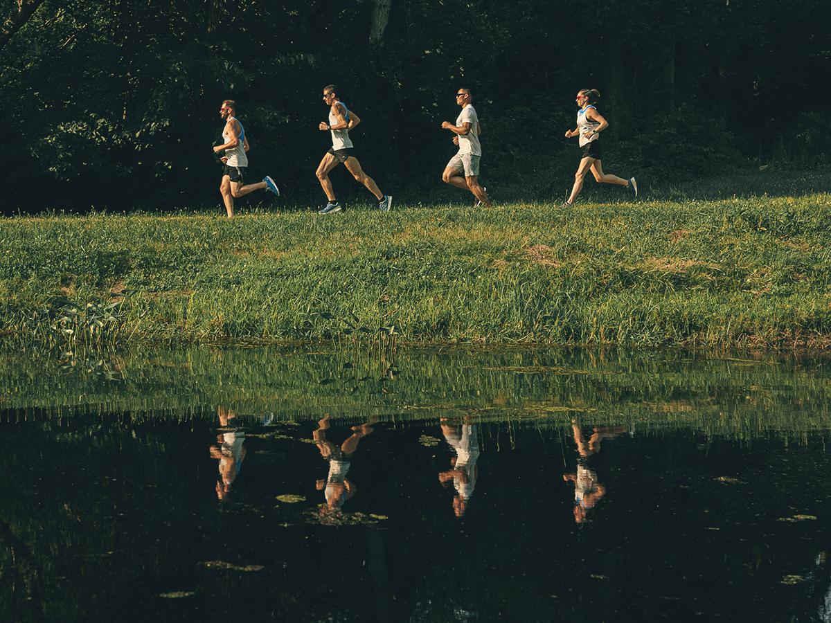 A group of four people running in a line along a lake.
