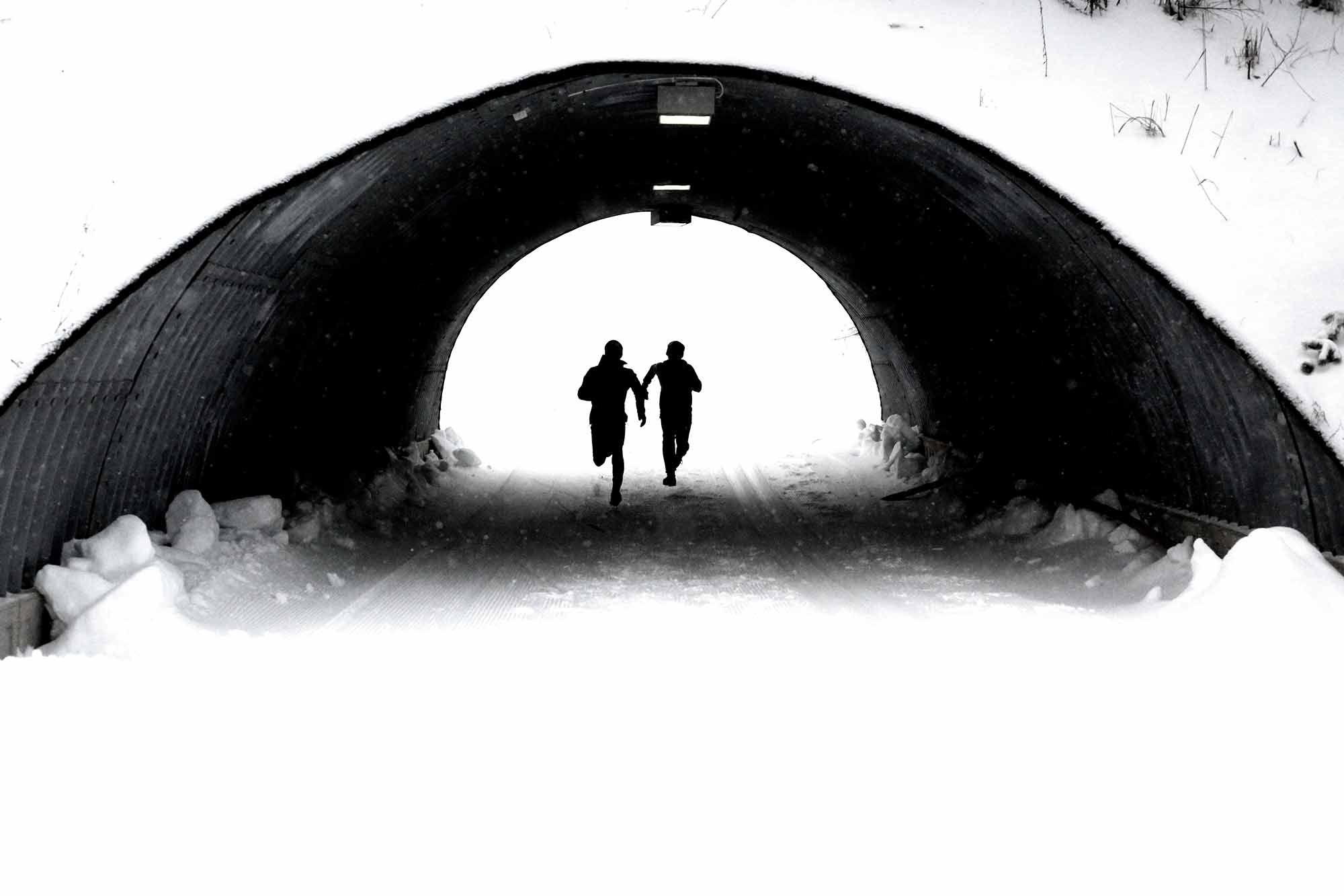 Two people running beneath a tunnel in the snow.